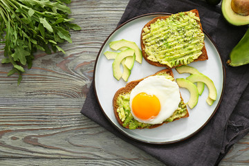 Plate with tasty avocado toasts on wooden table