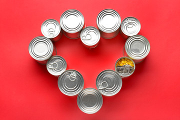 Heart shape made of tin cans with food on color background