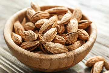 Bowl with unpeeled almond nuts on wooden background, closeup
