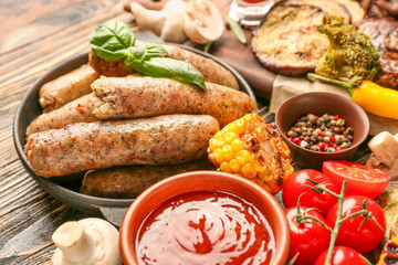 Frying pan with tasty grilled sausages and vegetables on wooden table