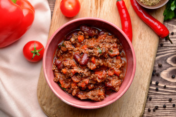 Bowl with tasty chili con carne on wooden board