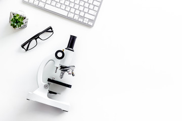 Medical tests on work desk of doctor with microscope, keyboard, glasses on white background top view copyspace