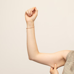 A closeup view of a young Caucasian lady squeezing her upper arm, showing the sagging skin and fat beneath the triceps, commonly referred to as bingo wings. Isolated against a white background.