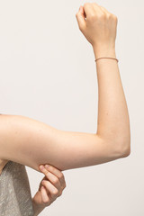 A close up view of a Caucasian woman squeezing her arm showing saggy muscles and skin in her upper arm, commonly referred to as bingo wings. Isolated with copy space above the arm.