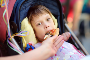 Mother feeding pizza's a little disabled girl in a wheelchair. Child cerebral palsy. Inclusion.