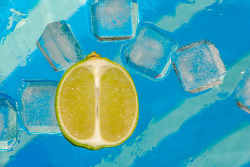 Slice of lime and ice cubes on blue background