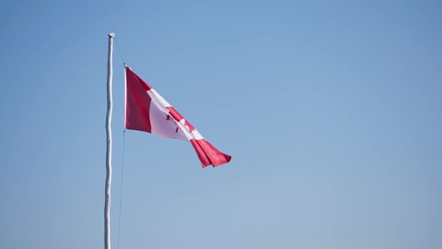 Canadian maple leaf flag waving in wind on wooden flag pole agianst a blue sky.