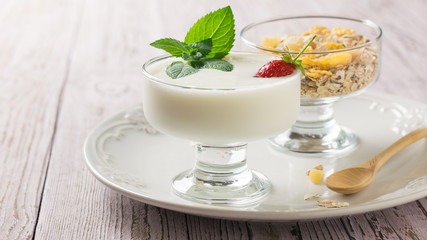 Bowl of yogurt and strawberries with mint and bowl of oatmeal on a wooden table.