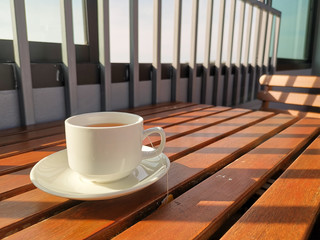 A cup of tea on wooden background. The sun shines on the table as a stripe. Morning tea time.