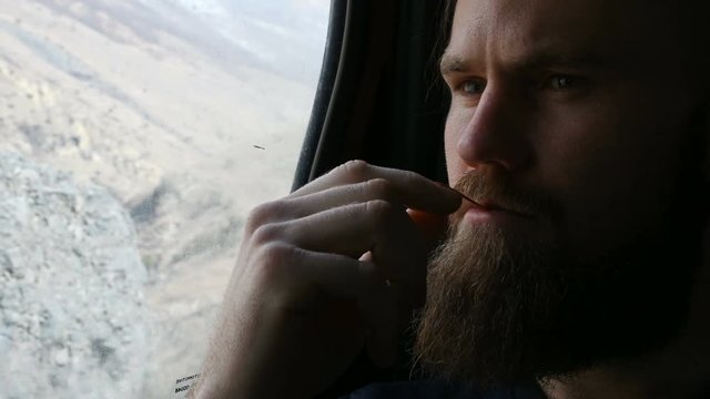 Close-up portrait of a talking bearded hipster male sitting in the car in the backseat and meditating on the sides against the background of mountains