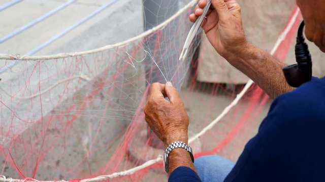 Old fisherman reparing fishing net during the day.