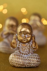 monk figurine.I do not see, I do not hear, I do not speak concept.small golden monk figurine set on golden background with  golden bokeh.The religion and the motto of life.Statues with emotions