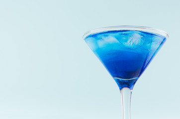 Glamour tropical fruit blue cocktail with curacao, ice cubes in misted martini glass in modern mint color background, top part, details.