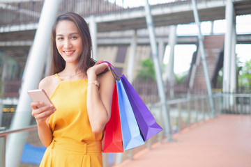 Beautiful women with shopping bags and smartphone enjoying in shopping standing outdoors of shopping mall, shopping concept