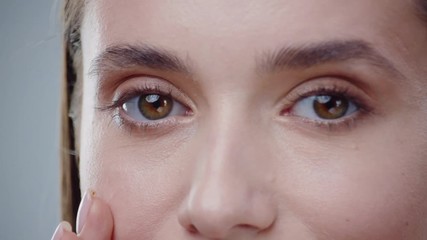 Close up face eyes young woman look at camera lead by hand on the face grey background care skincare female perfect studio adult attractive girl makeup model cute pretty portrait close up slow motion