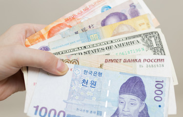 Naklejka premium A hand holding money banknotes of different countries: Korean won, Russian rouble, Dollar USA, Chinese RMB yuan and ukraine grivna