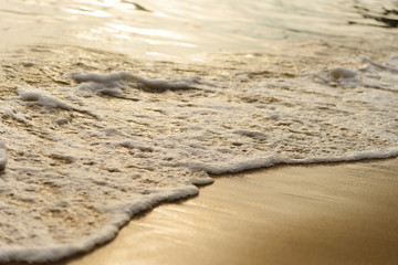 Golden light reflecting off a water wave at the sea and sand on sunset. Pure Gold