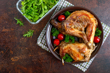 Whole baked rabbit with greens and tomatoes on a plate. Tasty dietary meat. Top view, flat lay.