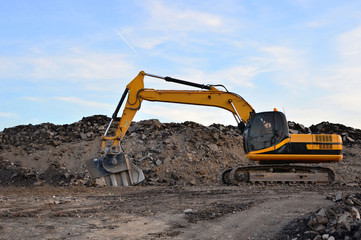 Fototapeta na wymiar A heavy excavator in a working at granite quarry unloads old concrete stones for crushing and recycling to gravel or cement. Special heavy construction equipment for road construction.