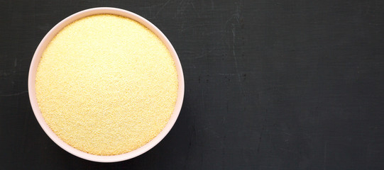 Dry semolina durum flour in a pink bowl over black surface, top view. Overhead, from above, flat lay. Space for text.