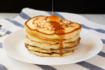 Homemade pancakes with butter and maple syrup on a white plate, side view. Closeup.