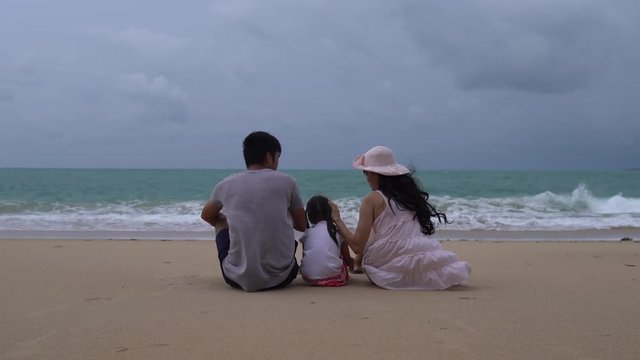 Happy Asian family sat together on the sandy beach admire the sea on summer holidays