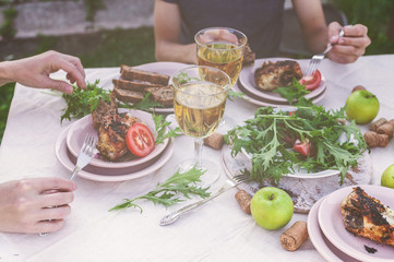 Dinner in the garden. People eat at the table with wine, grilled fish, fresh vegetables and herbs. Horizontal shot