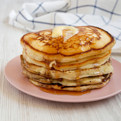 Homemade pancakes with butter and maple syrup on a pink plate, side view. Close-up.