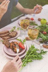 People eat at the table in the garden. Dinner at sunset with wine, grilled fish, fresh vegetables and herbs. Vertical shot