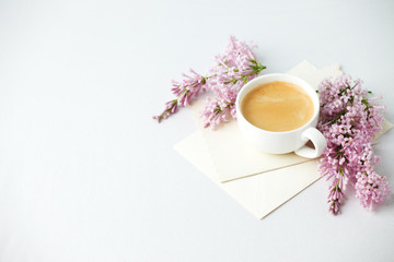 Minimal elegant composition with coffee cup and lilac branches, envelope on white background, female morning breakfast, woman mother day, saint valentine day