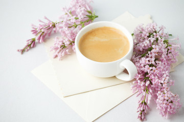 Modern still life with lilac flowers, envelope and cup of coffee, on white wbackground, copy space. Holiday or wedding background. minimalist style, female breakfast