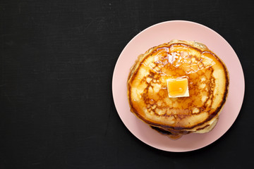 Homemade pancakes with butter and maple syrup on a pink plate, top view. Flat lay, top view, from above. Copy space.