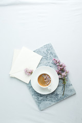 Obraz na płótnie Canvas Woman desktop elegant. Coffee cup and ililac branches on marble plate on white the table. Mock-up for artwork. View from above. Flat lay. Springtime famale concept