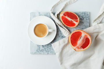 Stylish breakfast concept - cup of coffee, red grapefruit, tissue bag on mafble plate on white background, female modern minimal morning breakfast