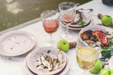 Glasses of white and rose wine, grilled fish plates, vegetables, salad and fruits on the table. Summer party in the backyard. Horizontal shot