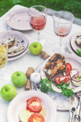 Glasses of white and rose wine, grilled fish plates, vegetables, salad and fruits on the table. Summer party in the backyard. Vertical shot