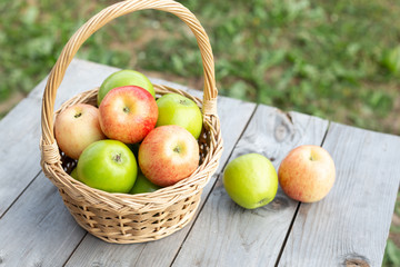 Green apple in wicker basket on wooden table Green grass in the garden Harvest time Organic food Rustic style