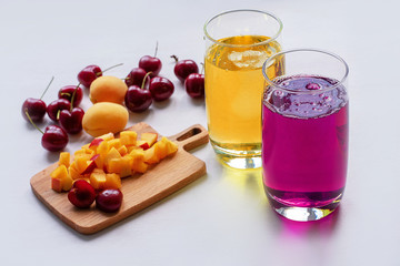 Apricot and cherry juice, apricots, cherry on a sunny table. Summer drinks and fruits. Juice in glass, cherry and apricot juice