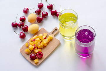 Apricot and cherry juice, apricots, cherry on a sunny table. Summer drinks and fruits. Juice in glass, cherry and apricot juice