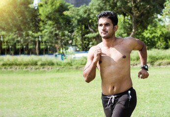 Young Indian athlete man practicing for his marathon race in sports ground. Athlete running on roadside in park.