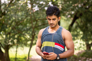 Portrait of young handsome man wearing red hat and using smartphone with headphone , Indian man portrait in outdoor location