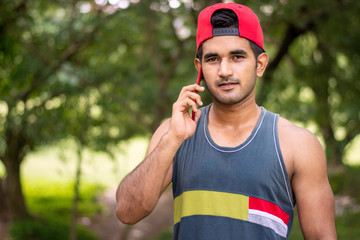 Fototapeta premium Portrait of young handsome man wearing red hat and using smartphone with headphone , Indian man portrait in outdoor location