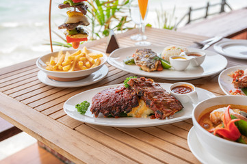 Variety of food, roasted pork ribs, beef steak, seafood and spicy soup on dining table