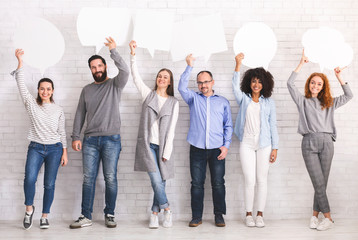 Naklejka premium Global communications. Group of happy young people holding empty speech bubbles and looking at camera while standing against grey background