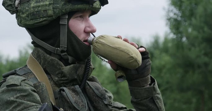 Soldier in camouflage drinks water from a military flask, quenches thirst.