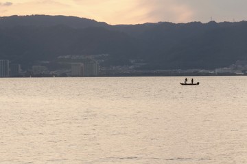 Naklejka premium 夕日に照らされた湖の上に浮かぶボートに乗って