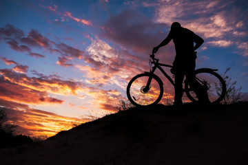 Fototapeta premium Silhouette of sports person cycling on the meadow on the beautiful sunset. Young man riding bicycle.