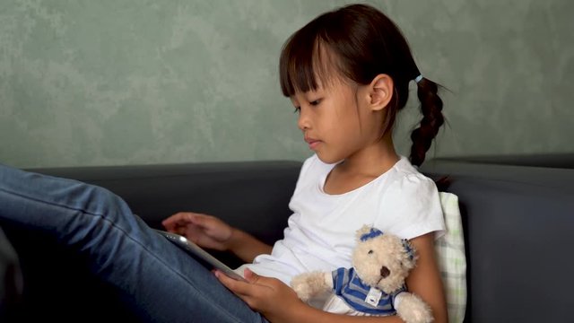 5 years old Asian girl Using tablet , watching cartoon, playing games on sofa in the living room