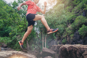 Crop Image of sport running man in cross country trail run jumping on the rocky mountain path.