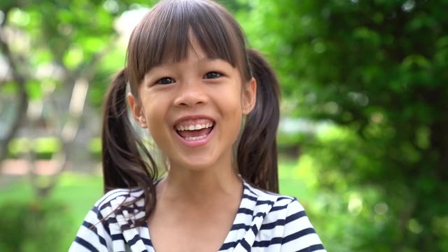 Slow motion of 5 years old Asian girl smiling and laughing happily in green park background